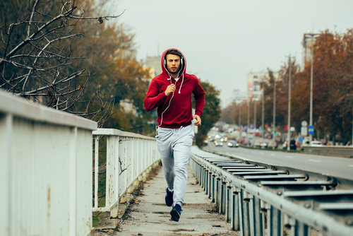 Man in red hoodie jogging beside the road in the city