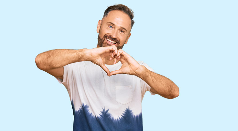 Handsome middle age man wearing casual tie dye tshirt smiling in love doing heart symbol shape with hands. romantic concept.