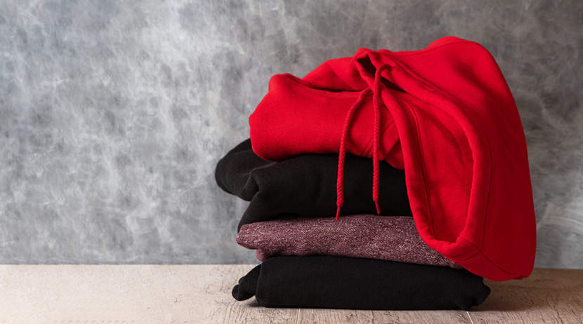 Stack of hooded sweatshirts and hoodie on gray background. Copy space