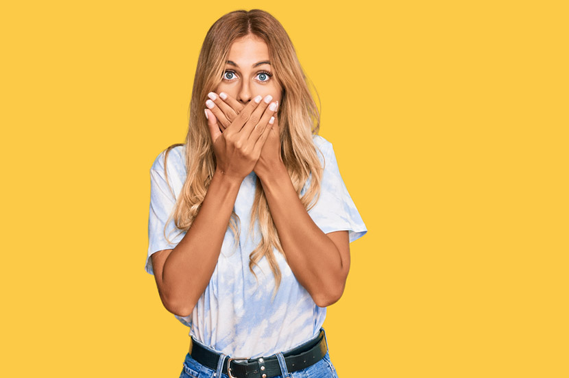 Beautiful blonde young woman wearing casual tie dye shirt shocked covering mouth with hands for mistake. secret concept.